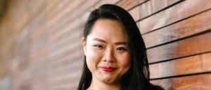 Young dark-haired Asian woman leaning on a wooden wall.